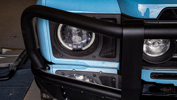 Detailed view of the heavy-duty bullbar protection over the INEOS Grenadier LED headlights, highlighting the textured powder coat and precision fit.