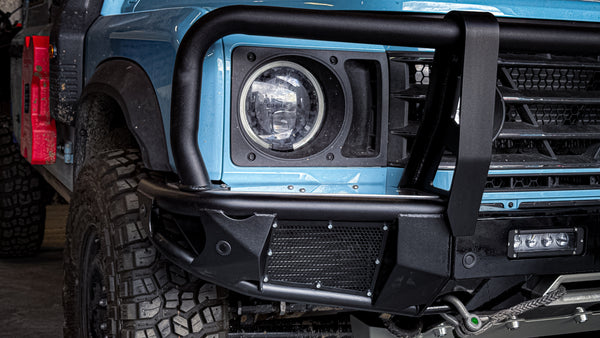 Corner view of the INEOS Grenadier front bumper highlighting the protective mesh inserts, laser-welded steel wings, and auxiliary light mounting.