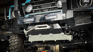 Low angle view of the INEOS Grenadier front protection system highlighting the mega-duty aluminum skid plate and the high-strength steel bumper construction for maximum off-road clearance.
