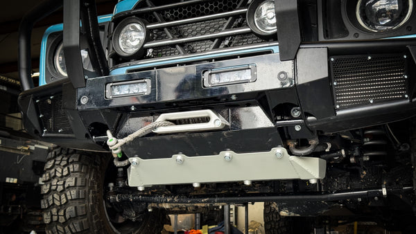 Low angle view of the INEOS Grenadier front protection system highlighting the mega-duty aluminum skid plate and the high-strength steel bumper construction for maximum off-road clearance.