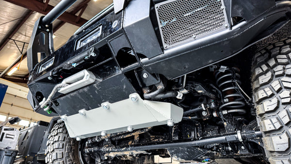 Low-angle shot of the INEOS Grenadier front protection system, showcasing the reinforced lower crossbar, mega-duty skid plate, and high-clearance design for off-road suspension